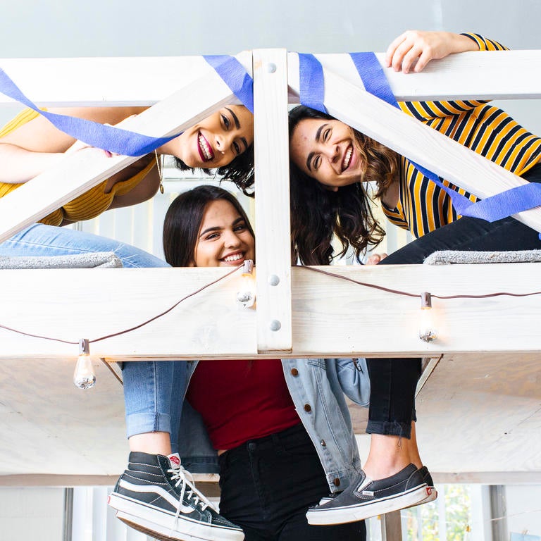 Three students smiling in a lofted dorm area